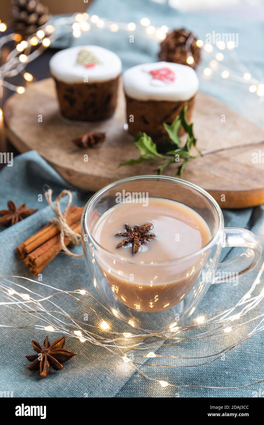 masala Tee und süße Kuchen auf einem Tisch mit Weihnachtsdekoration. Masala Chai ist ein indisches Teegetränk, das durch Kochen von schwarzem Tee in Milch und Wasser mit einer Mischung aus aromatischen Kräutern und Gewürzen hergestellt wird Stockfoto
