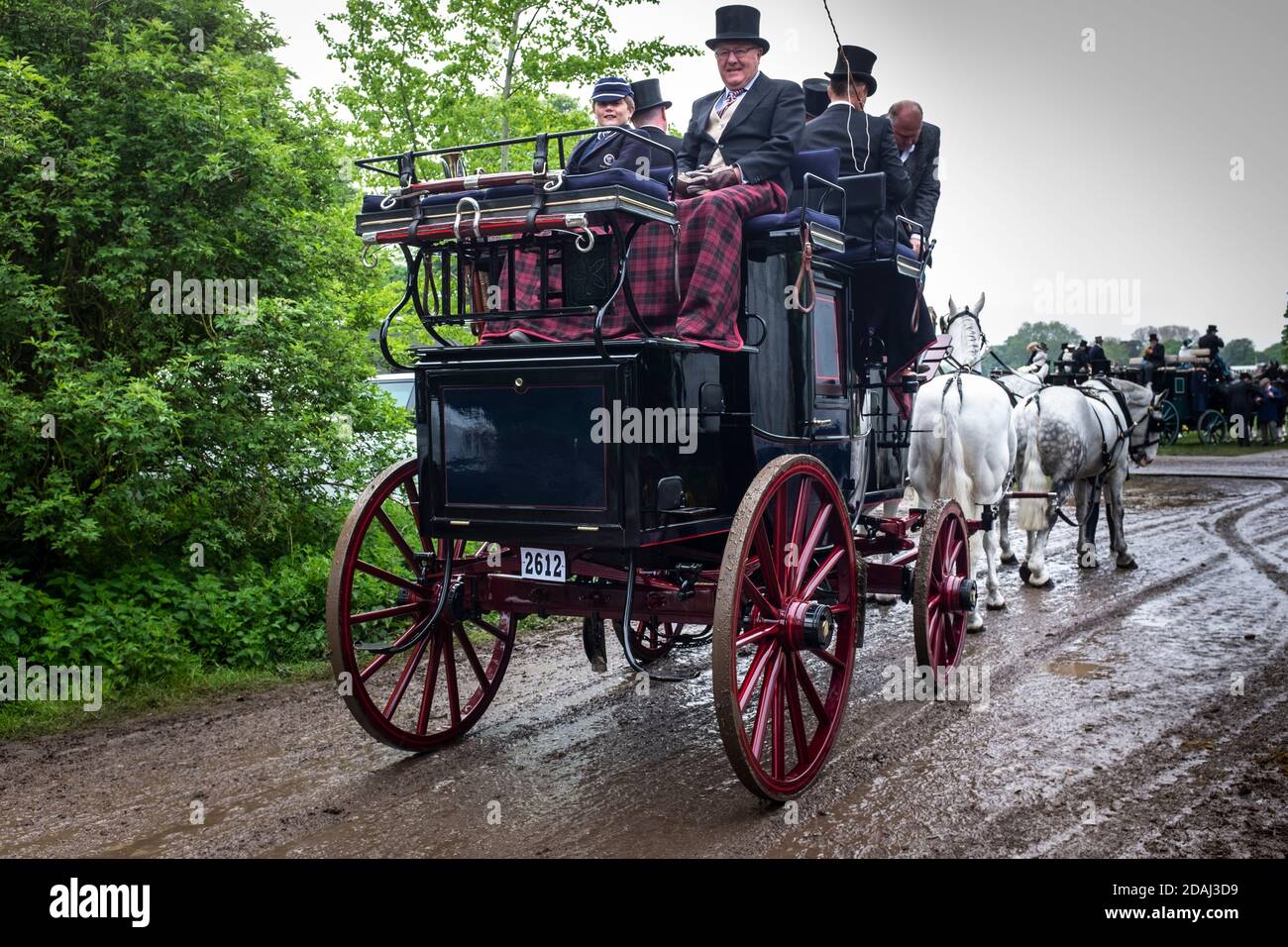 Ein alter 'Reisebus und vier' mit Fahrern und Passagieren, die während einer ziemlich nassen Royal Windsor Horse Show in England angemessen in historischen Kostümen gekleidet waren. Stockfoto