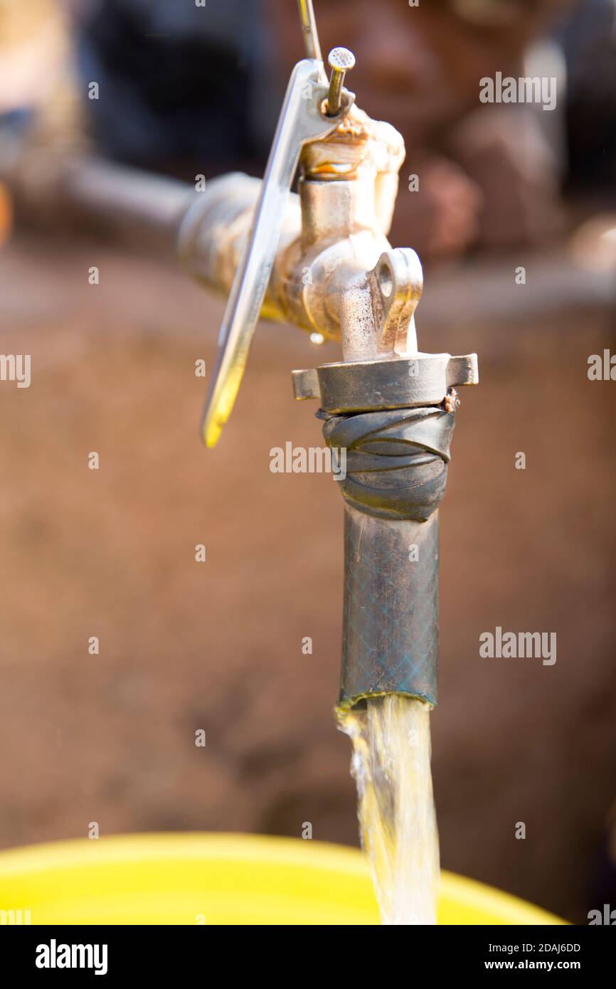 Selingue, Mali, 25. April 2015; EIN Wasserhahn an der Hauptstraße. Frauen und Mädchen, die Wasserbehälter füllen, konkurrieren mit den Motorradreinigern um Wasser. Stockfoto