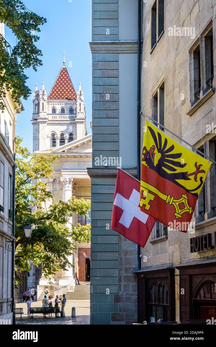 Der nördliche Glockenturm der Kathedrale Saint-Pierre in Genf, durch eine enge Straße in der Altstadt gesehen, mit Flaggen über einem Hotel. Stockfoto