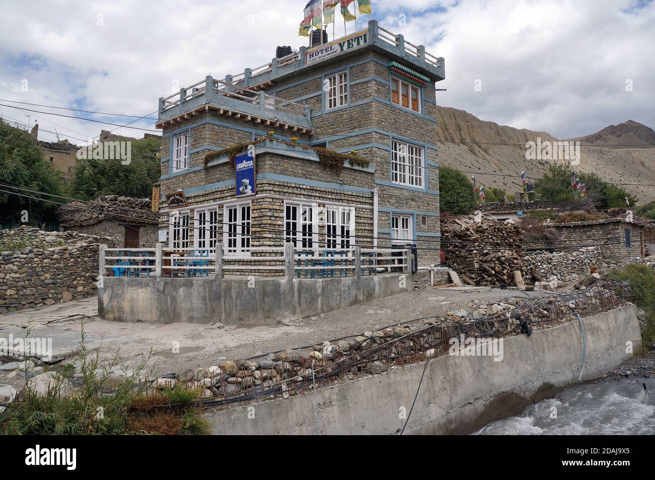 Das zweistöckige Yetti Hotel liegt am Ufer des Flusses vor der Kulisse der Himalaya-Berge in der Jomsom-Stadt Mustang, Nepal. Stockfoto