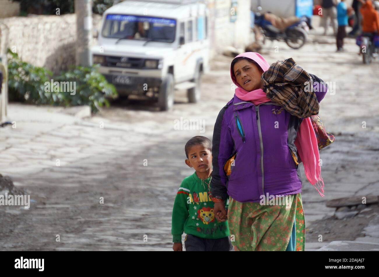Eine nicht identifizierte Frau indischer Nationalität trägt eine Tasche und führt ein Kind entlang der Jomsoma Street in Nepal, Mustang District. Stockfoto