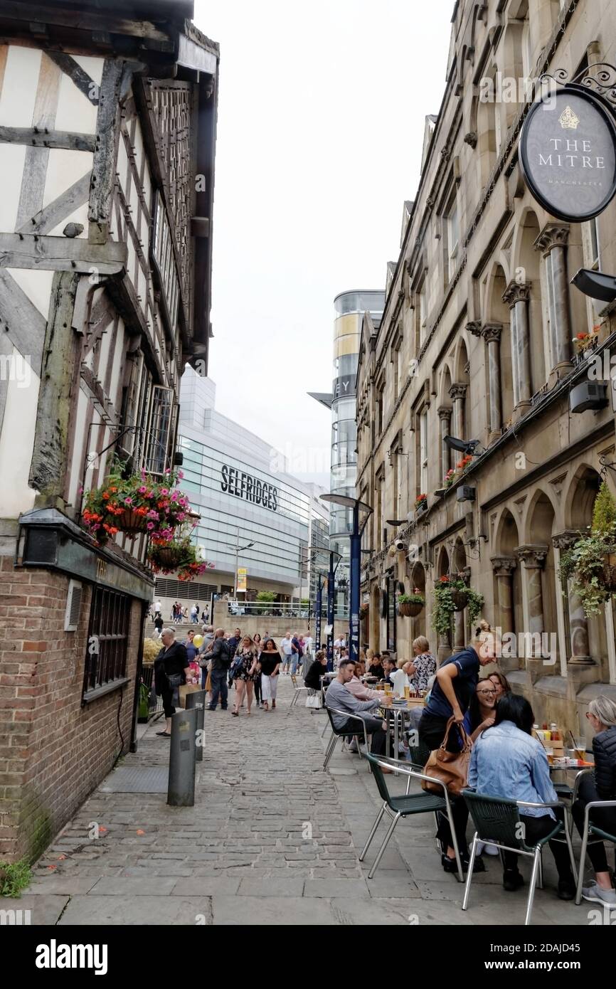 Blick auf die Cathedral Gates im Zentrum von Manchester, vorbei an den Kneipen Mitre und Old Wellington und Restaurants im Freien zum Selfridges & Co Store. Stockfoto