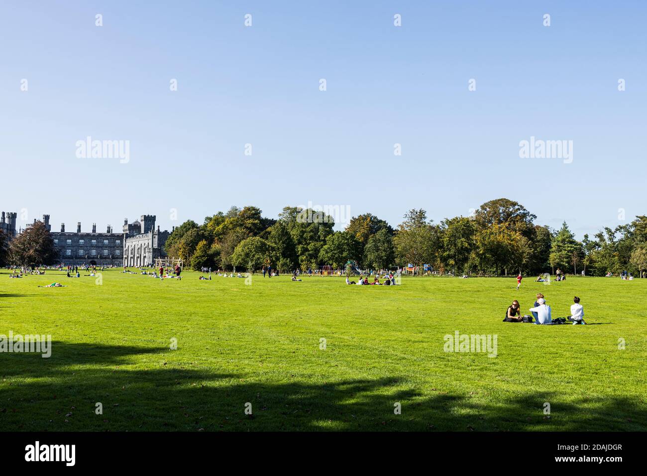 Menschen, die das sonnige Wetter auf dem Rasen auf dem Gelände der Burg Kilkenny, County Kilkenny, Irland, genießen Stockfoto