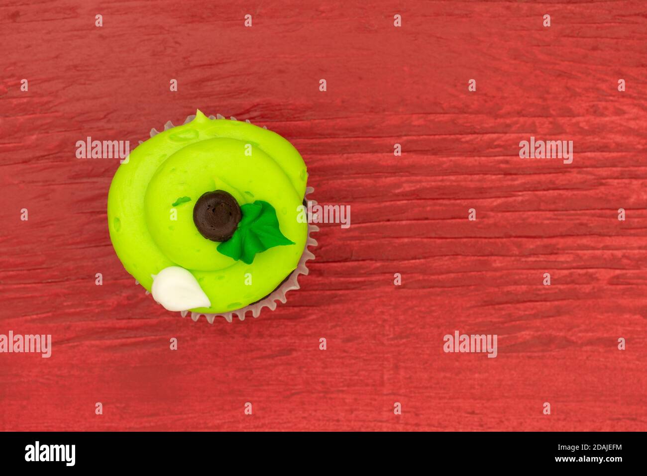 Draufsicht auf einen hell matt dekorierten grünen Cupcake auf einem rot lackierten Holzhintergrund. Stockfoto