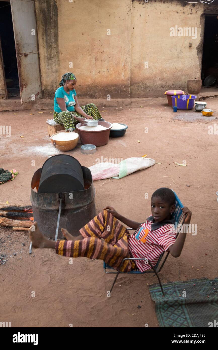 Selingue, Mali, 26. April 2015; der Haushalt von Camara. Der Junge, der Erdnüsse röstet, ist der 7-jährige Seydou Doumbia, der für Taschengeld von 100 CFA arbeitet. Fanta Doumbia siebt Maismehl, um es zu verkaufen. Nakani Troure, Ehefrau von Bogory Camara, röstet ebenfalls Erdnüsse. Erdnüsse verkaufen sich schnell und sind daher eine gute Einkommensquelle. Die Familie kam aus Dalaba Koro (alt Dalaba), wo der Damm im Jahr 1980 gebaut wurde. Bogory ist 51. Er sagt, dass der Damm eine Menge Infrastruktur mit sich bringt, aber die Familie hatte kein Land, um Nahrung anzubauen. 1983 bekam er einen Hektar Reis, 1985 einen Hektar Mais, und zwar an Stockfoto