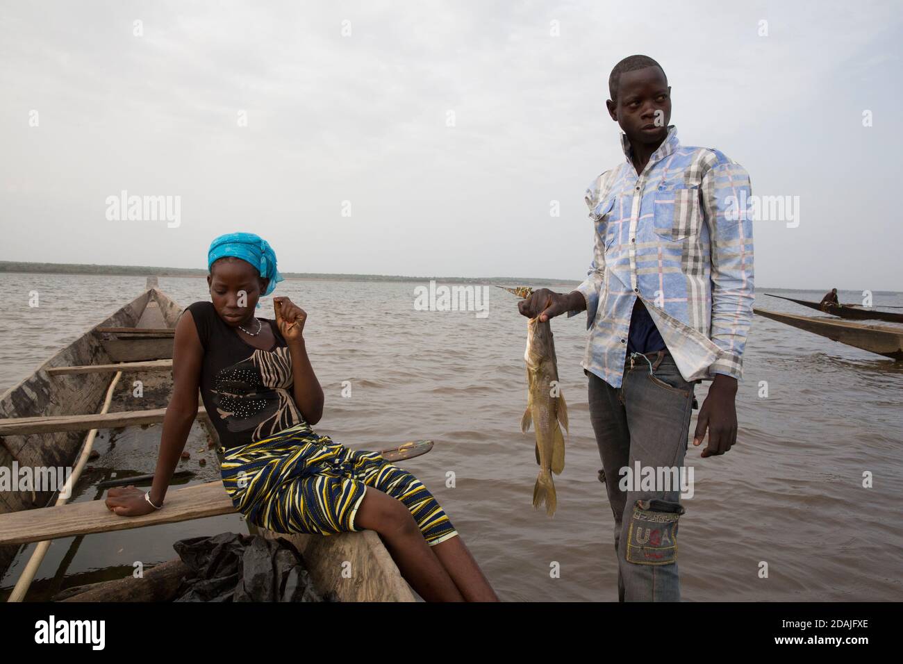Selingue, Mali, 27. April 2015; Tidiane Tienta, 15, Ist ein Speerfischer. Das Mädchen, das gekommen ist, um Fisch zu kaufen, ist Ramata Sidibe, 15. Sie ist frisch verheiratet und hat noch keine Kinder. Die Fische sind für die Menschen, die daran arbeiten, ihr neues Haus zu bauen und sie will für sie kochen. Sie zahlte 1000 CFA für 1 Kilo Fisch. Stockfoto