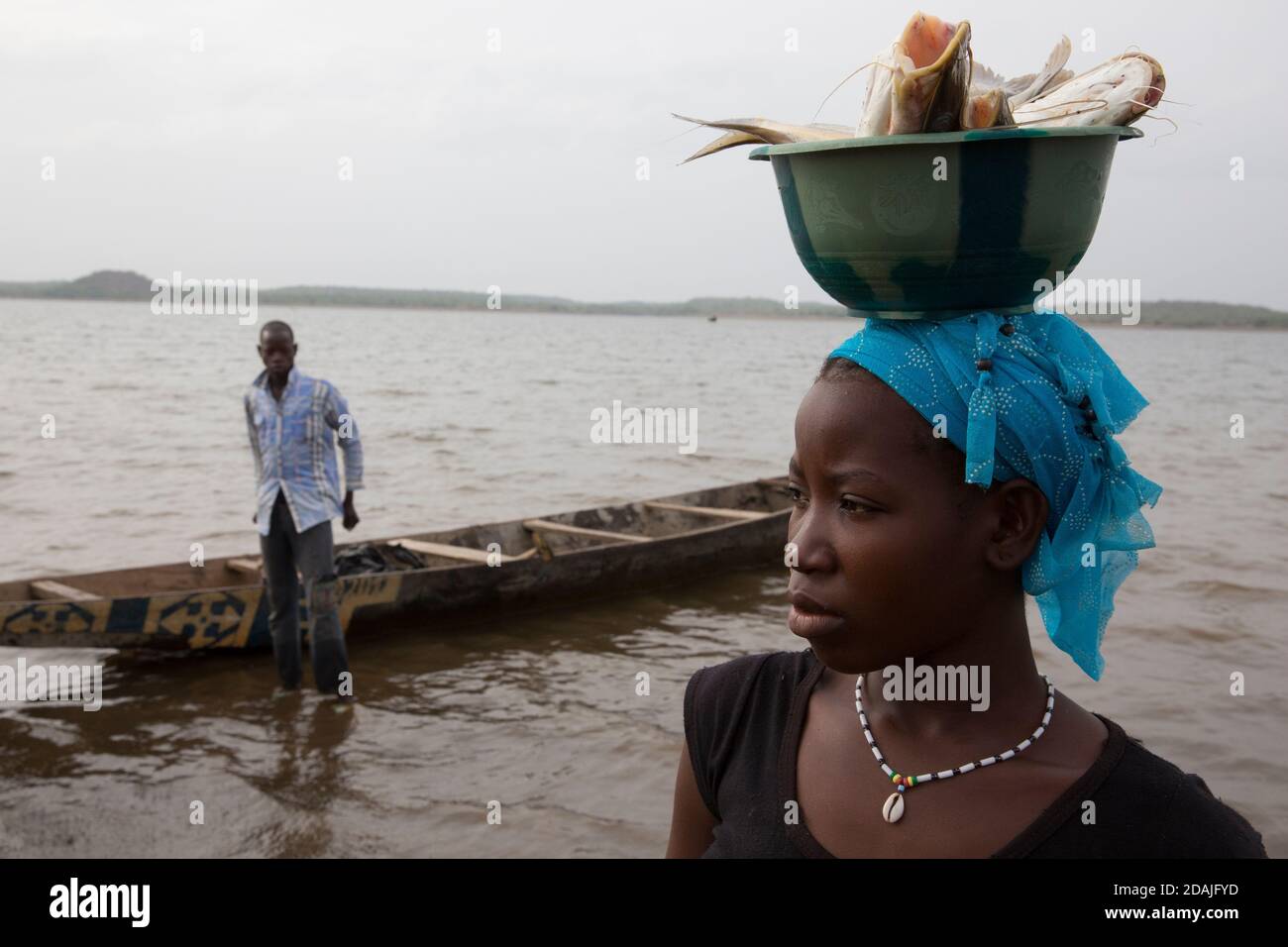 Selingue, Mali, 27. April 2015; Tidiane Tienta, 15, Ist ein Speerfischer. Das Mädchen, das gekommen ist, um Fisch zu kaufen, ist Ramata Sidibe, 15. Sie ist frisch verheiratet und hat noch keine Kinder. Die Fische sind für die Menschen, die daran arbeiten, ihr neues Haus zu bauen und sie will für sie kochen. Sie zahlte 1000 CFA für 1 Kilo Fisch. Stockfoto