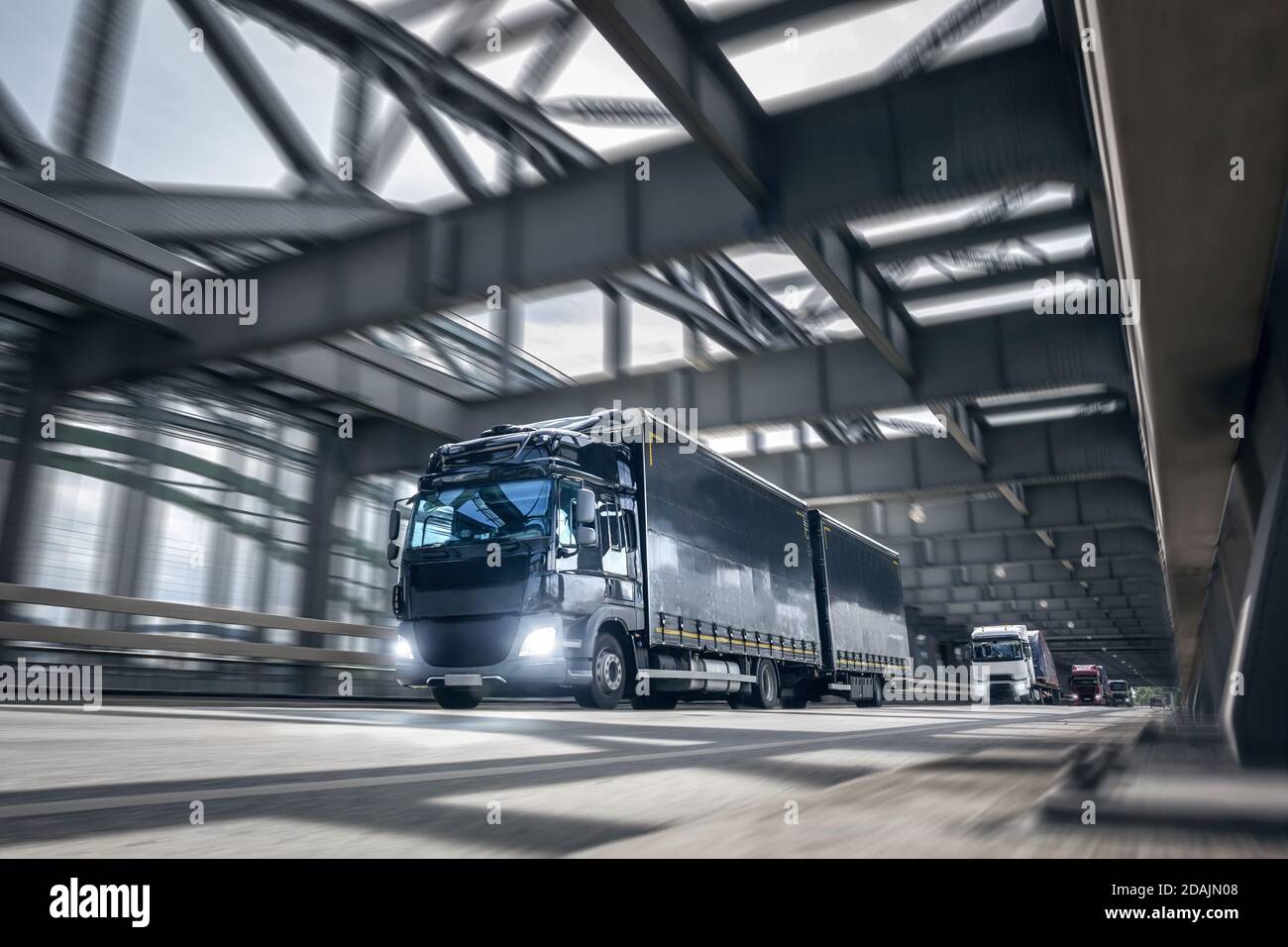 Mehrere LKWs fahren über eine Brücke in einem Industriegebiet Stockfoto