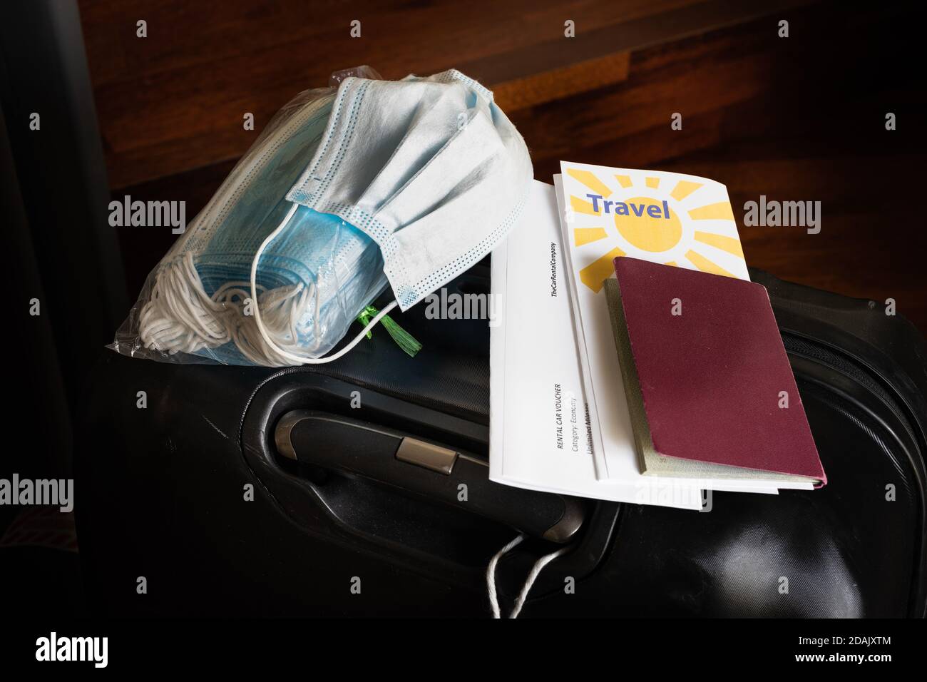 Reisen in Zeiten des Corona-Virus-Konzepts: Ein dunkler Koffer mit einer Packung Masken, einer gebrauchten Maske, Pass und Reisedokumente auf der Oberseite. Stockfoto