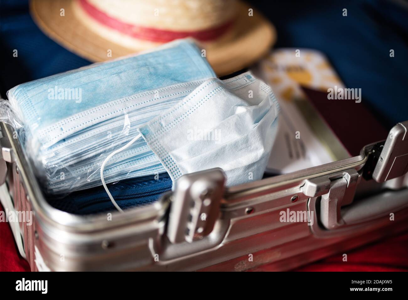 Reisen in Zeiten des Corona-Virus-Konzepts: Ein offener Koffer mit einer Packung Masken, einer gebrauchten Maske, einem Sonnenhut, einem Pass und Reisedokumenten. Stockfoto