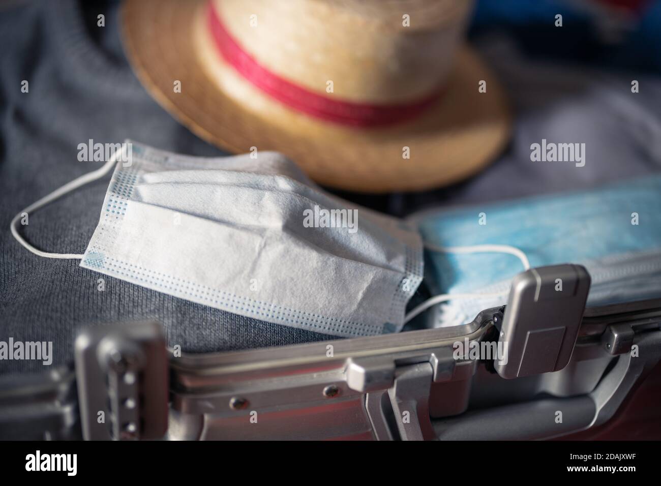 Reisen in Zeiten des Corona-Virus-Konzepts: Ein offener Koffer mit einer Packung Masken, einer gebrauchten Maske und einem Sonnenhut. Stockfoto