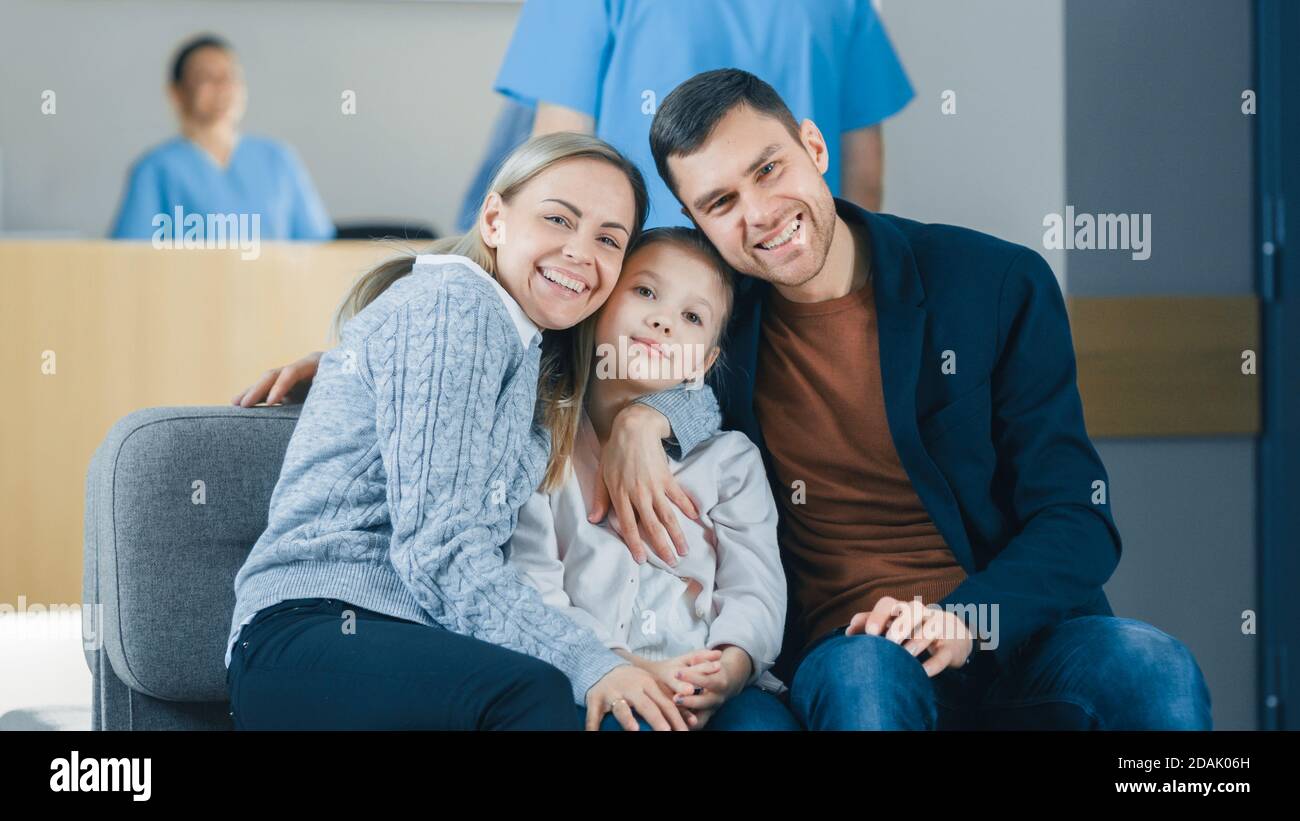 Porträt der jungen glücklichen Familie im Krankenhaus. Schöner Vater, schöne Mutter und nette kleine Tochter sitzen in der Lobby des Medical Stockfoto