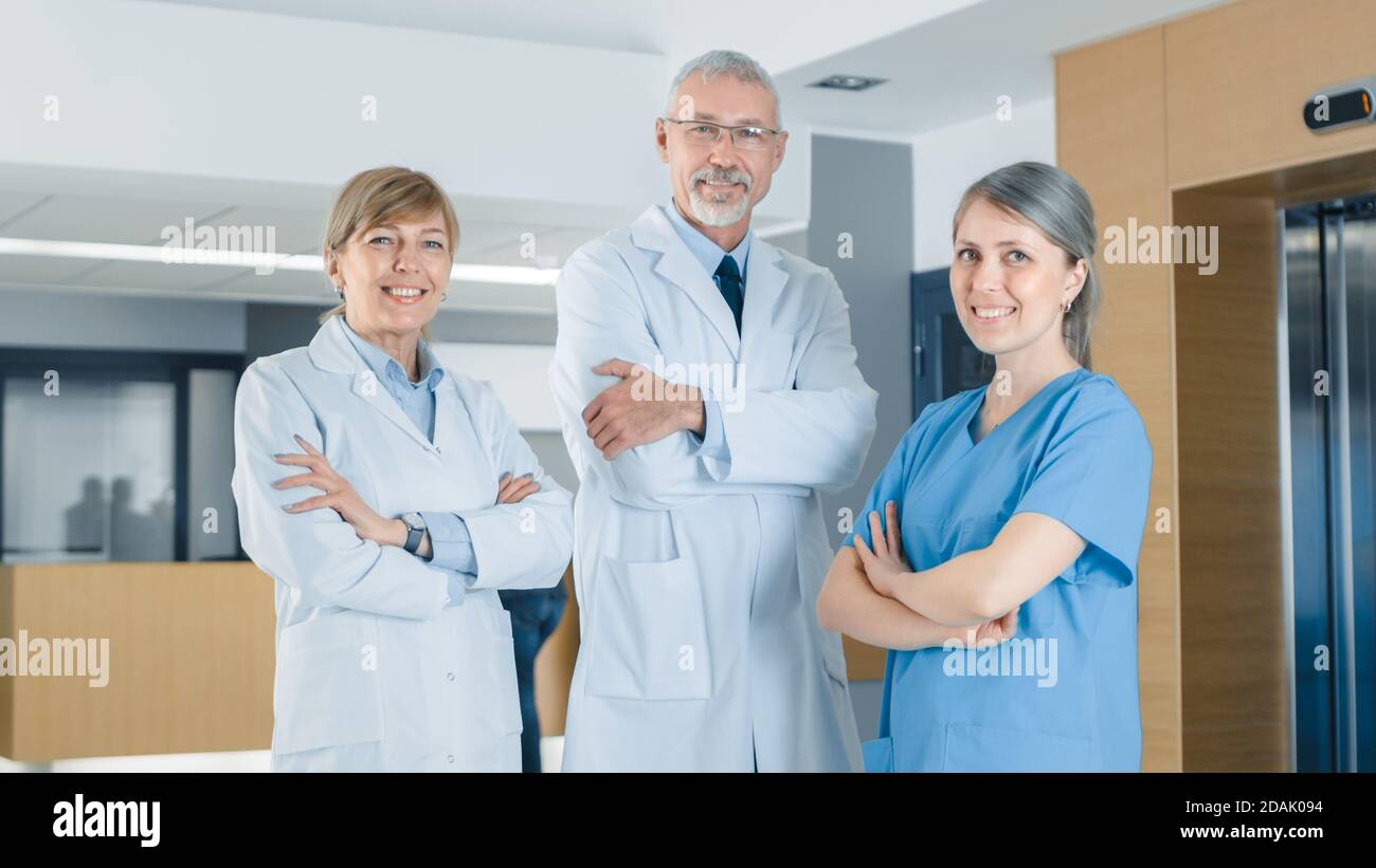 Porträt von zwei Ärzten und einer Krankenschwester, die im Krankenhausgebäude posiert, Arme gekreuzt und lächelnd. Brillante Menschen in medizinischen Profis, die sparen Stockfoto