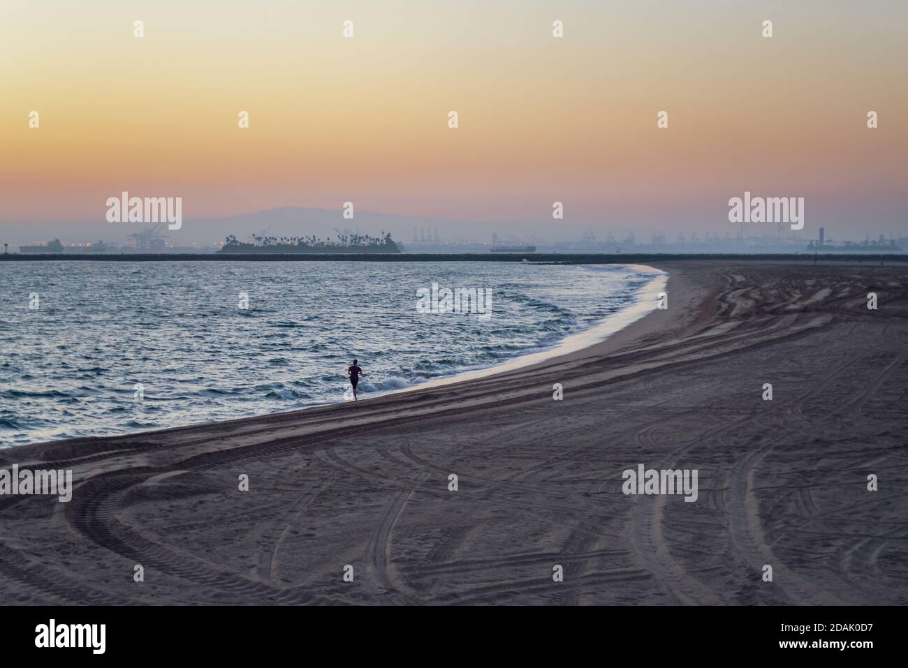 Ein junger Mann, der bei Sonnenuntergang am Huntington Beach läuft Stockfoto