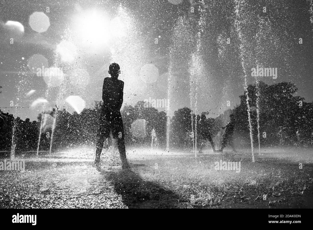 Silhouette eines Teenagers, der in einem Brunnen steht und die kühlen Wasserströme genießt. Glückliche Kinder spielen an einem heißen Tag in einem Springbrunnen Stockfoto