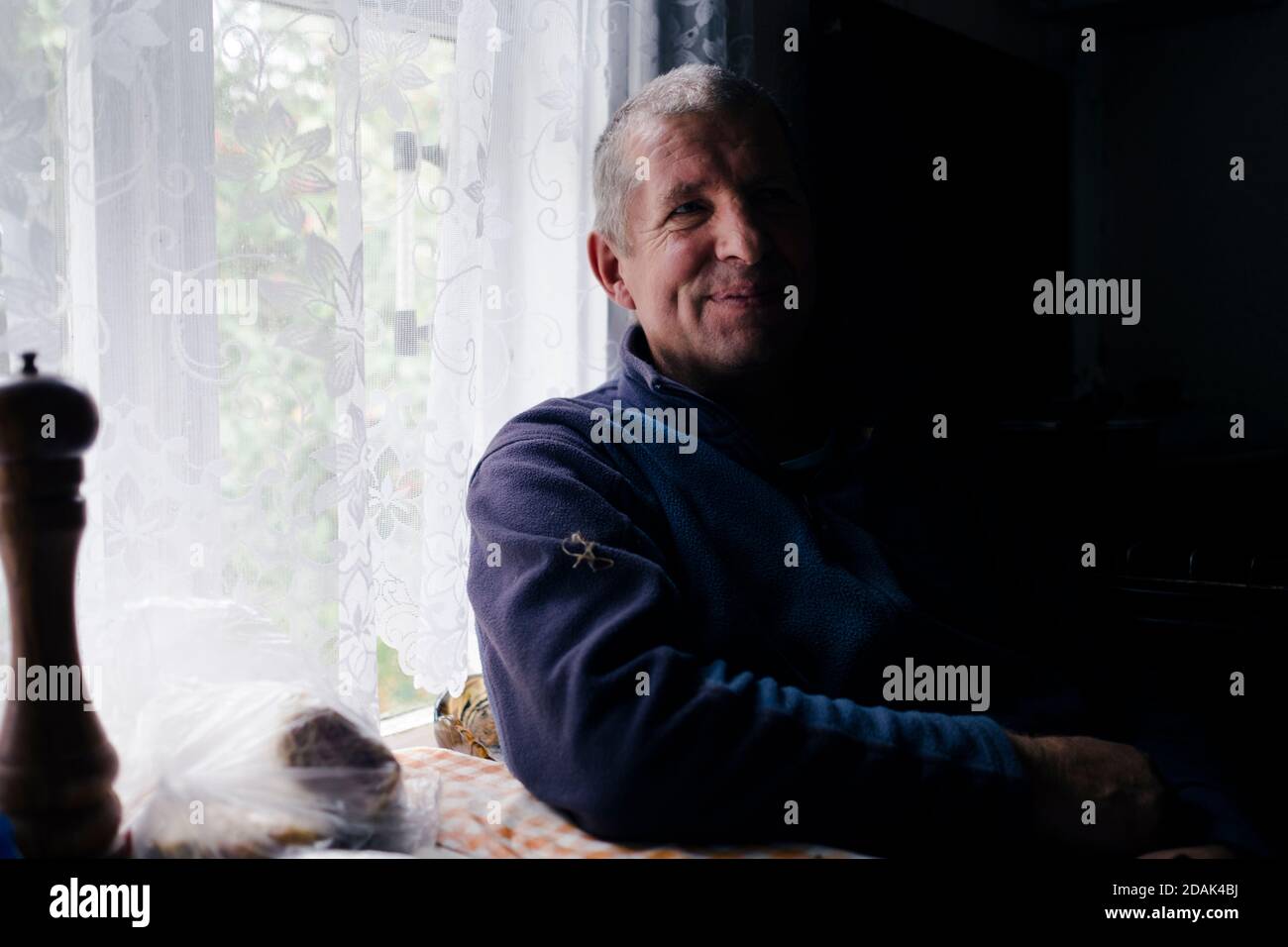 Ein Mann sitzt am Fenster; Schatten fällt auf die Hälfte seines Körpers und seines Gesichts. Stockfoto