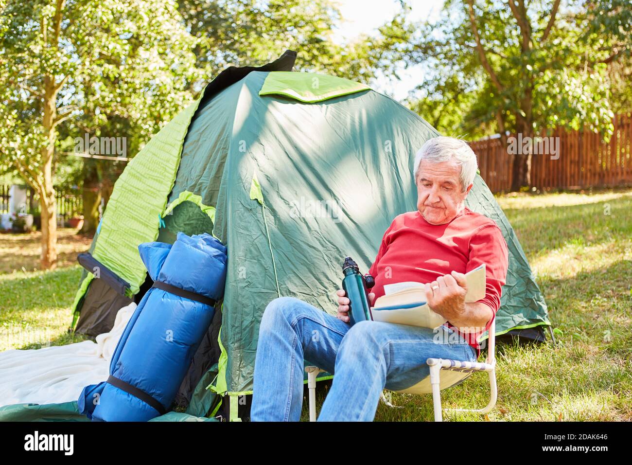 Entspannender älterer Mann im Campingstuhl beim Lesen vor dem Hotel Des Zeltes in der Natur Stockfoto