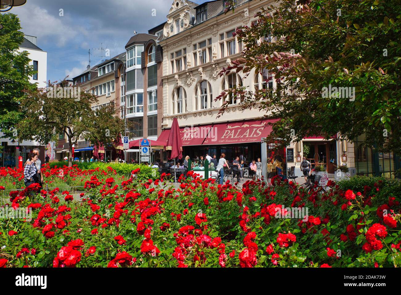Ein großes Blumenbett aus roten Blumen mit einem Straßenrestaurant im Hintergrund in der Stadt Koblenz in der Nähe des Rheins, Deutschland Stockfoto