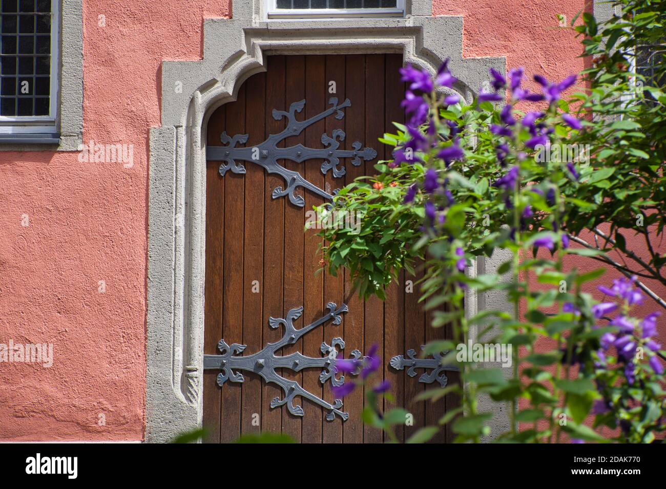 Eine hübsche alte Holztür mit großen verzierten Scharnieren und mit blauen Blumen draußen, in Koblenz, Deutschland Stockfoto
