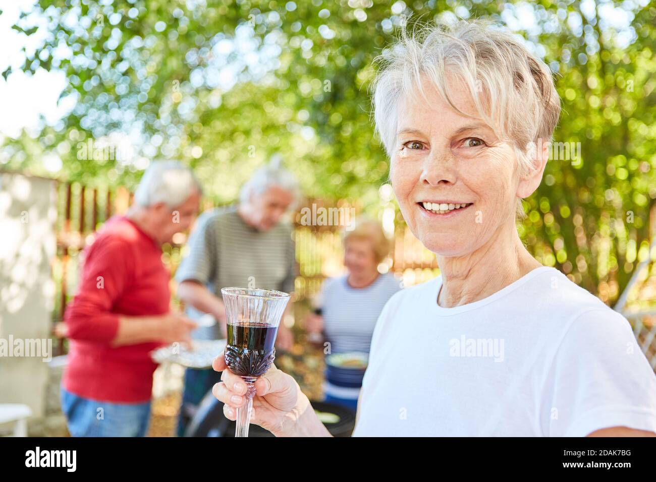 Lächelnde ältere Frau mit einem Glas Rotwein Eine Sommer Grillparty Stockfoto