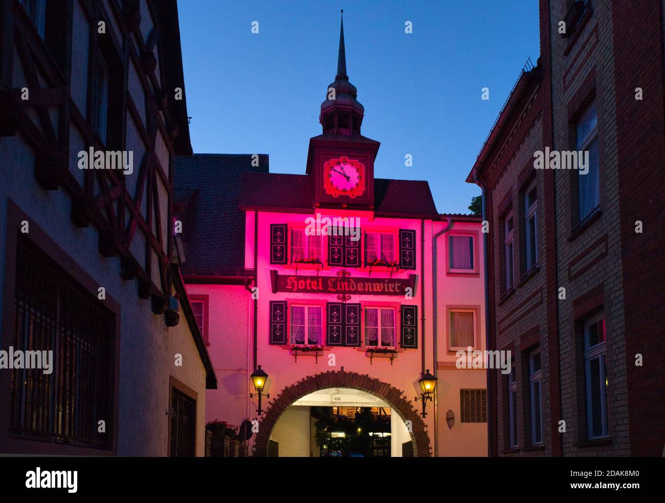 Ein hübsches Gebäude mit einem Uhrenturm oben und Torbogen unten, beleuchtet in der Dämmerung in Rüdesheim. Am Rhein, Darmstadt, Heese, Deutschland Stockfoto