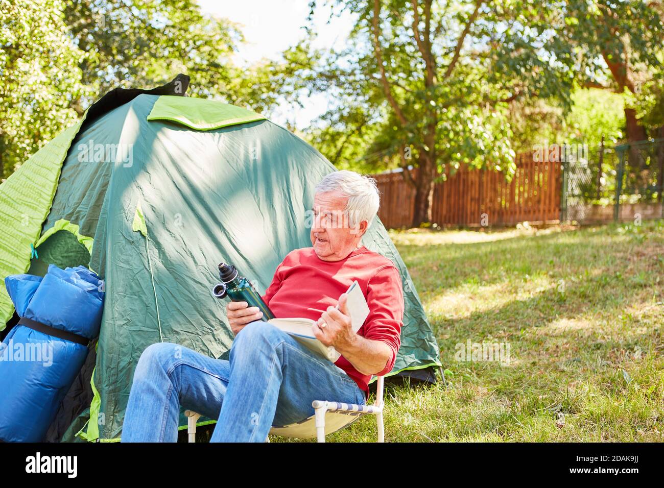 Senior vor dem Zelt beim Lesen im Campingstuhl beim Camping im Sommer Stockfoto
