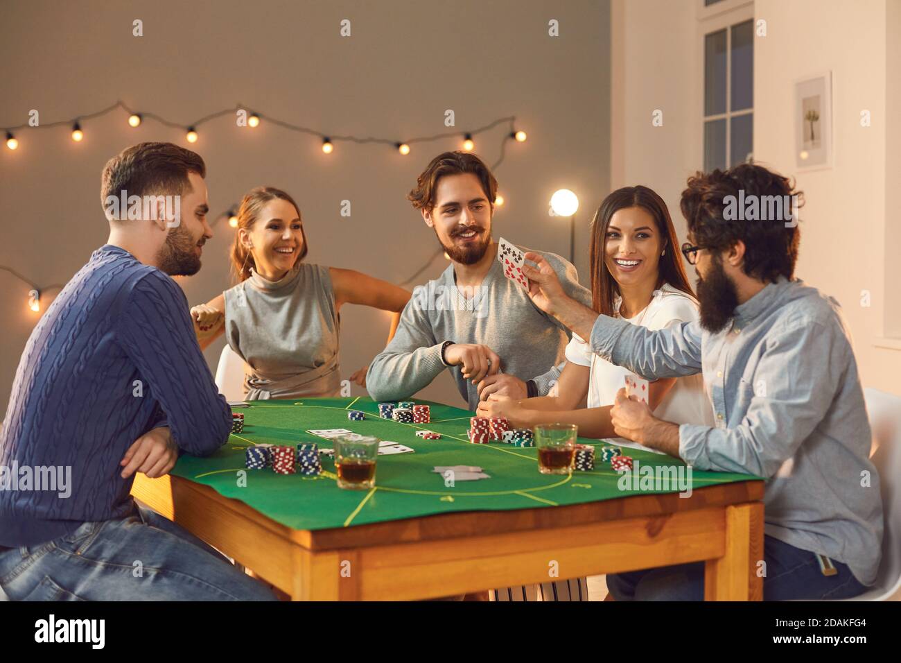 Gruppe von fröhlichen Freunden Wetten, Trinken und Poker spielen auf dem Tisch zu Hause Stockfoto