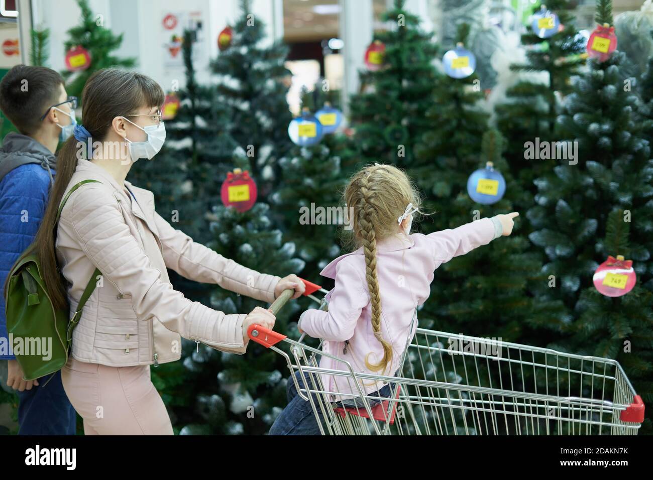 Mutter mit Kindern tragen Gesichtsmasken kaufen weihnachtsbaum in Das Einkaufszentrum Stockfoto