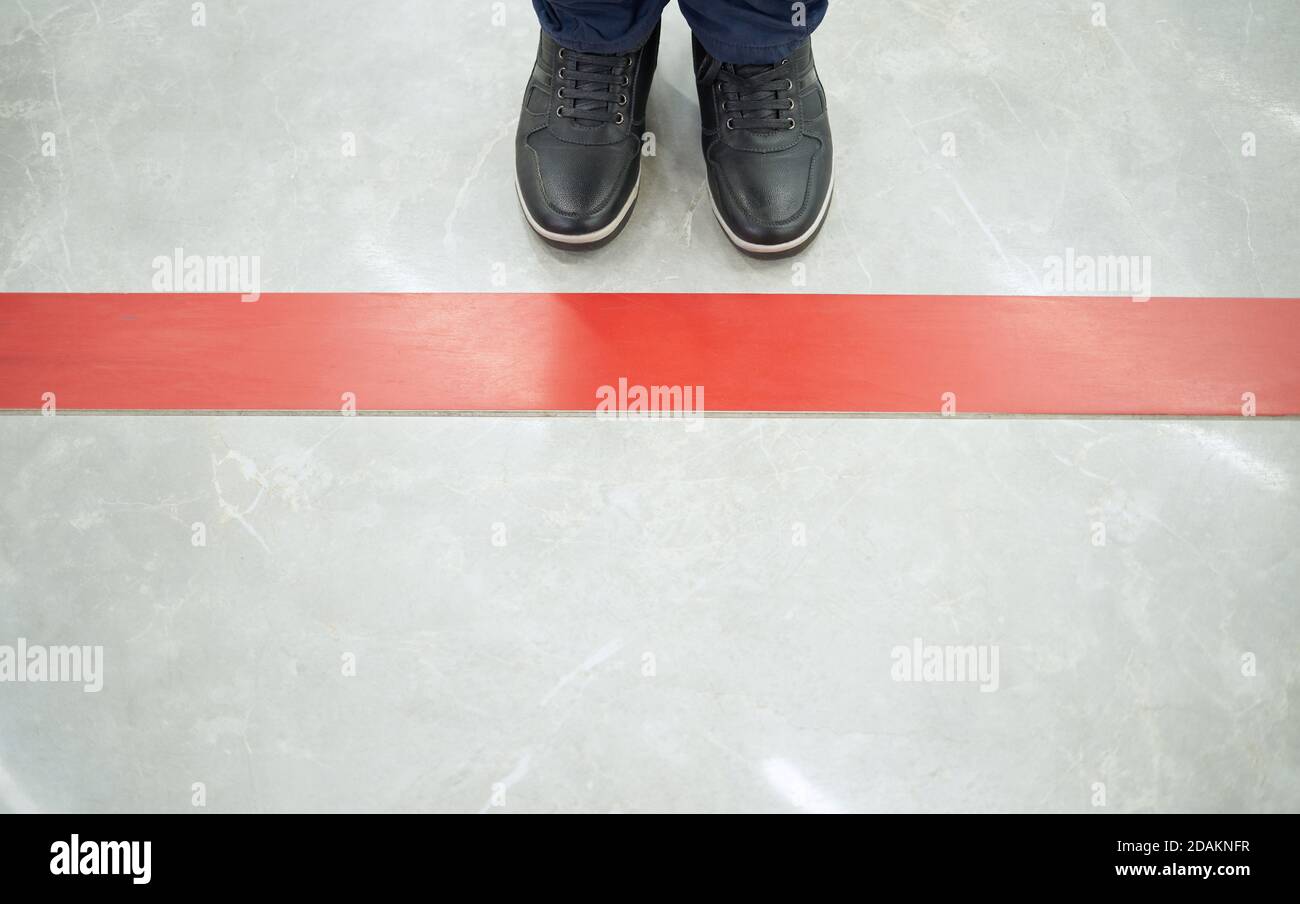 Eine Person steht an der roten Linie auf dem Boden In einem Einkaufszentrum mit sozialer Distanz Stockfoto