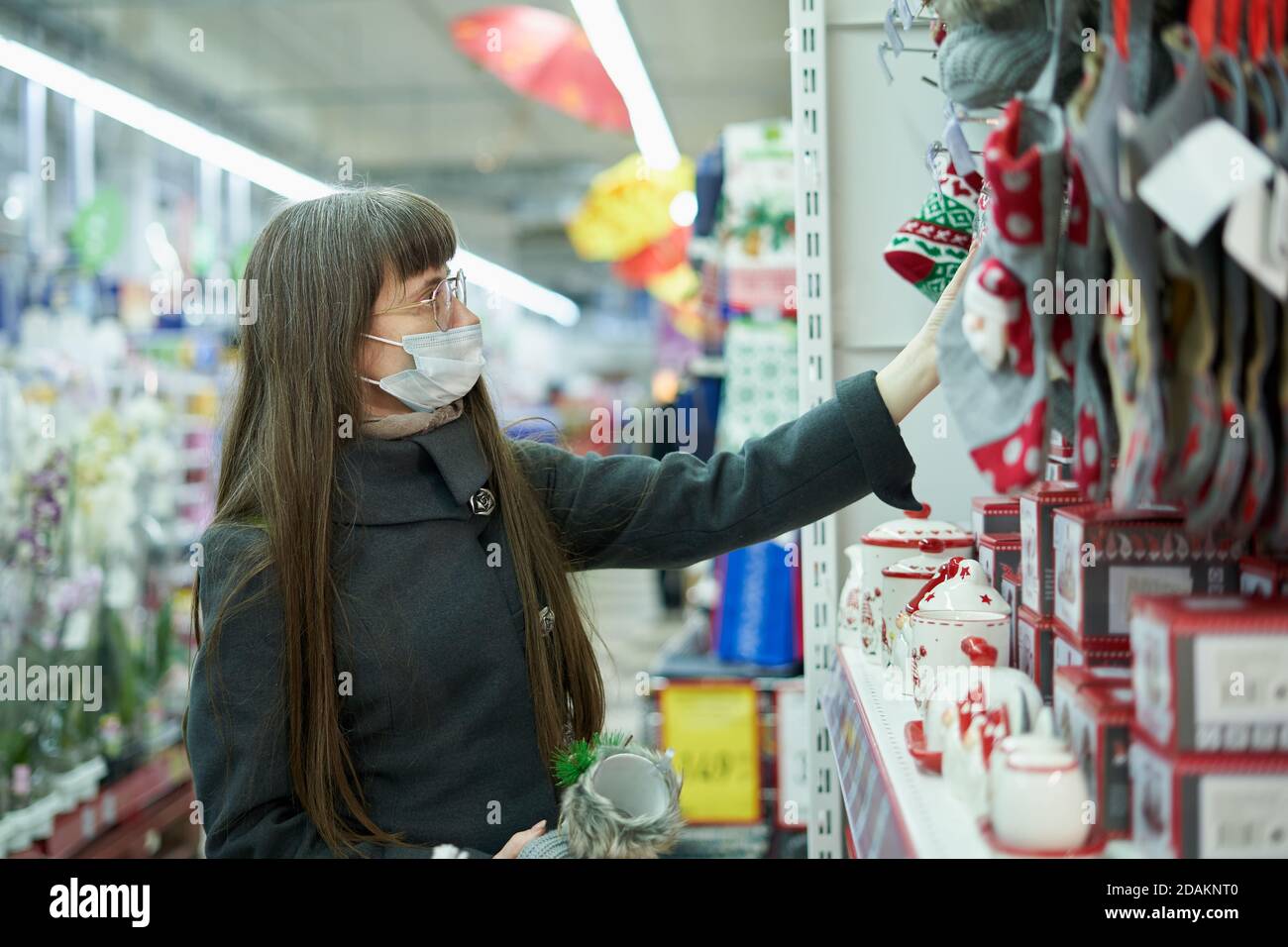 Junge Frau im Gesicht Maske wählt weihnachtsartikel auf der Regal im Laden zum Einkaufen Stockfoto