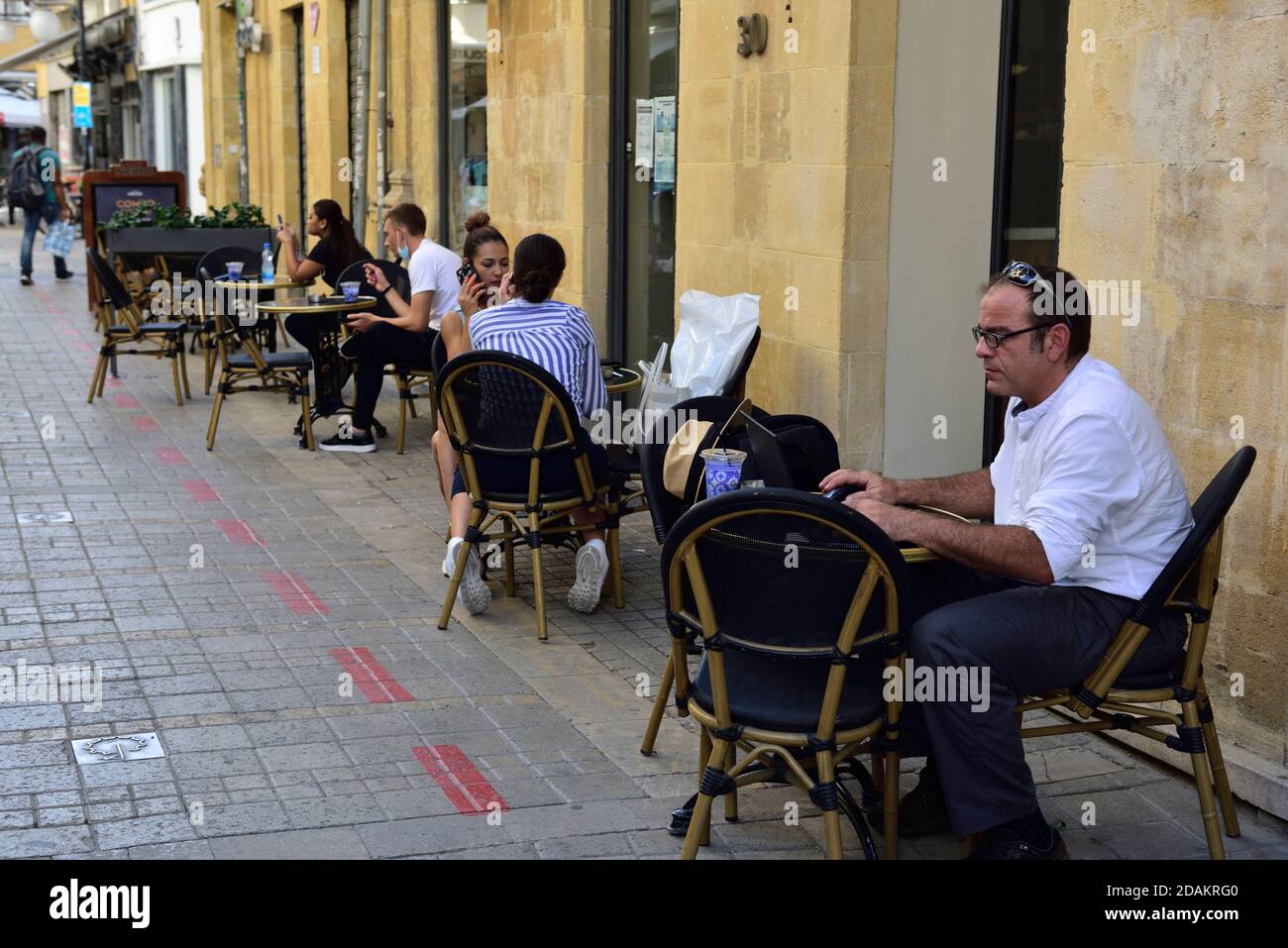 Straße in der Altstadt Nicosia mit Restaurant-Tische aus sozial distanziert auf Bürgersteig, Kunden auf Laptop oder im Gespräch Stockfoto