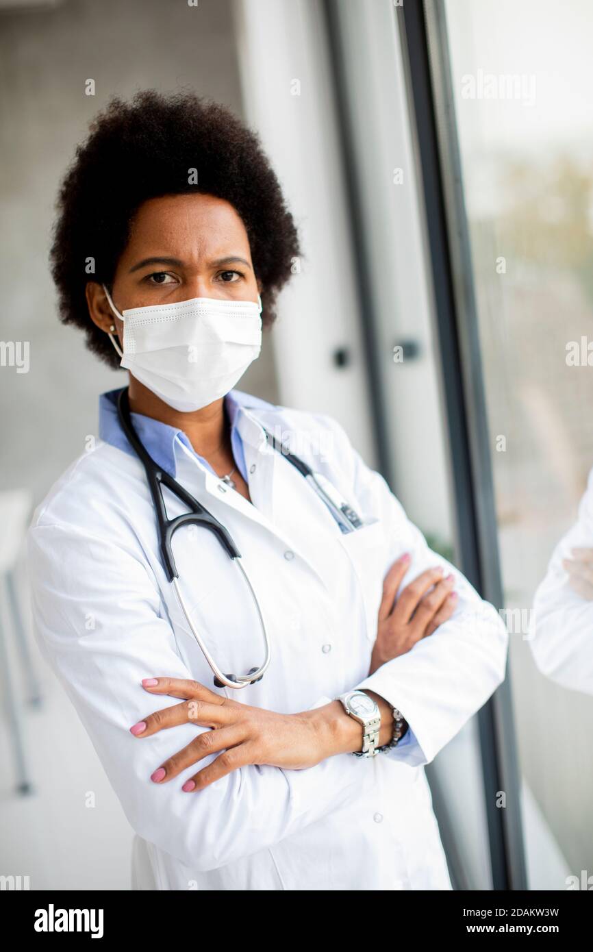 Schwarze Ärztin steht neben dem Arztpraxis Fenster mit Gesichtsschutzmaske Stockfoto