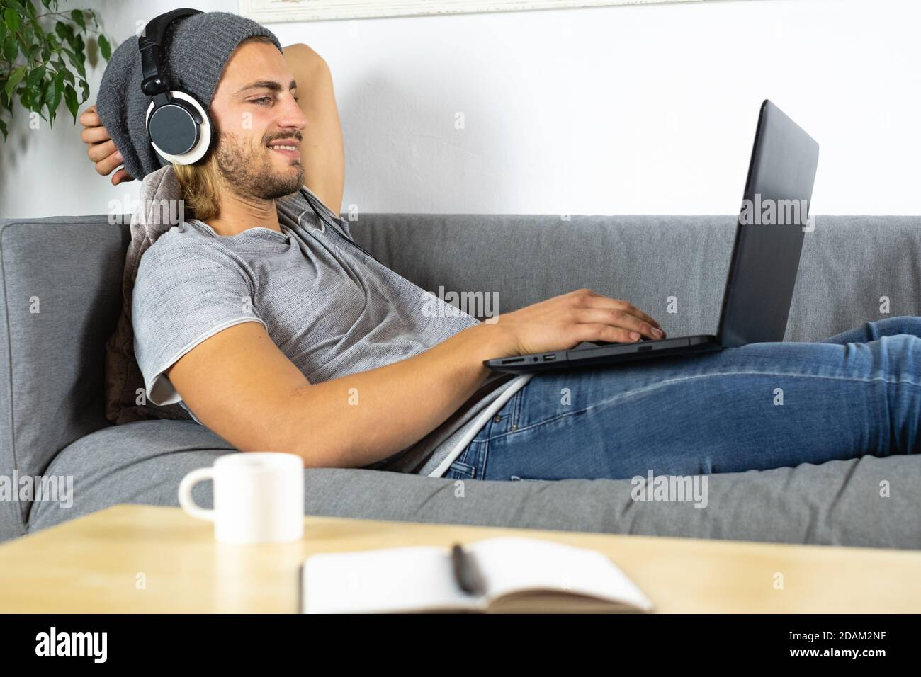Hübscher junger Geschäftskaukasischer Mann, der zu Hause mit einem Laptop arbeitet Und sich entspannt mit dem Handy unterhalten Stockfoto
