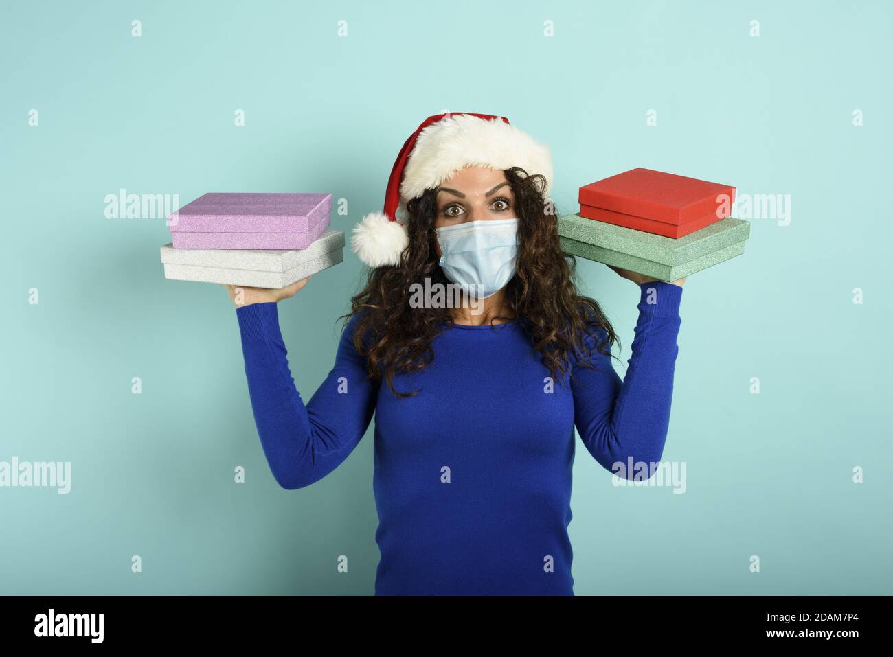 Glückliches Mädchen mit Gesichtsmaske erhält Weihnachtsgeschenke. Cyan Hintergrund Stockfoto
