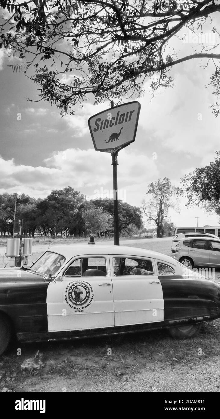 Fredericksburg, Texas - 12. Nov. 2020 Old Antique 1950 Hudson Police Car geparkt neben 1950s Sinclair Oil Corporation Gas-Schild in schwarz und weiß. Stockfoto