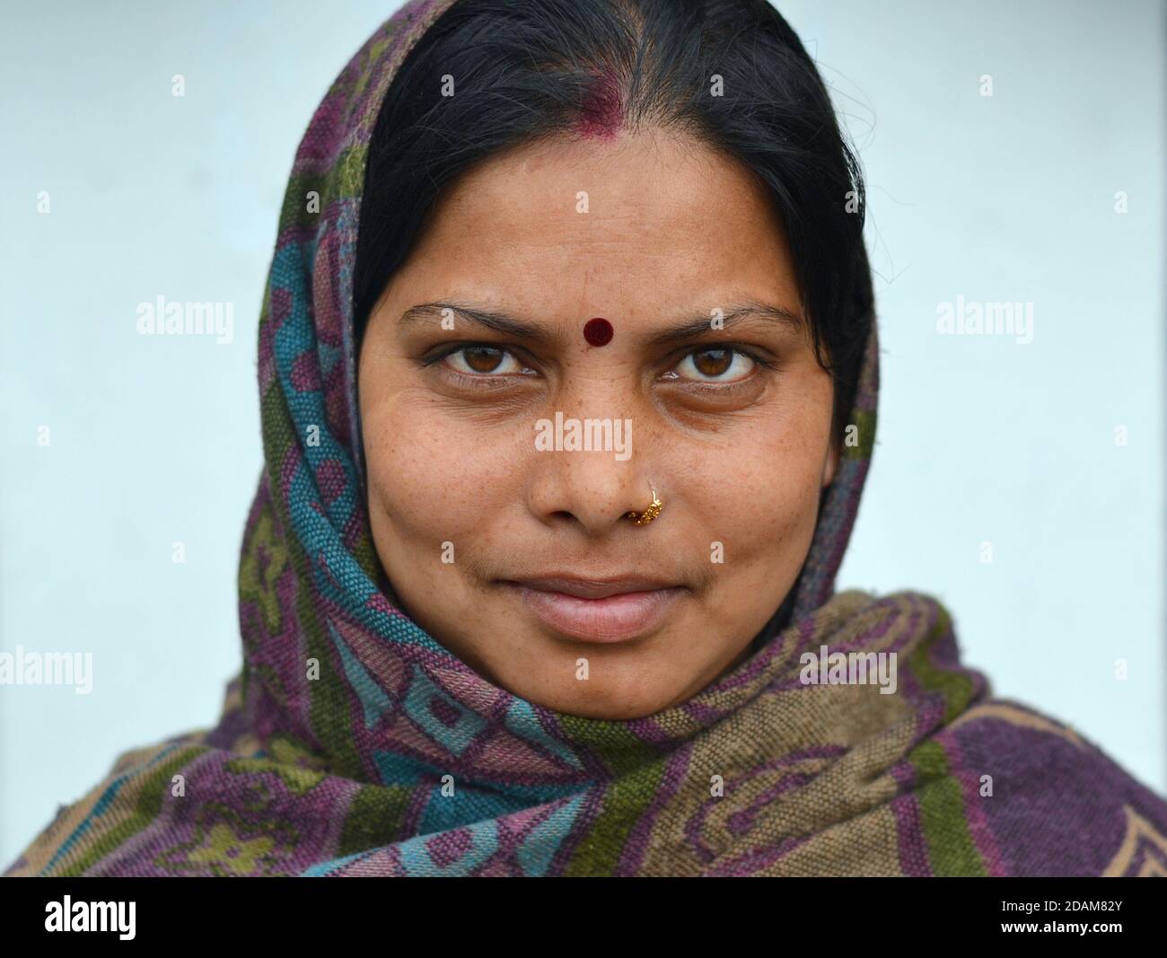 Verheiratete junge indische Hindu-Frau mit rotem Sindoor, rotem Bindi und goldenem Nasenring bedeckt ihren Kopf mit einem warmen Schal und posiert für die Kamera. Stockfoto