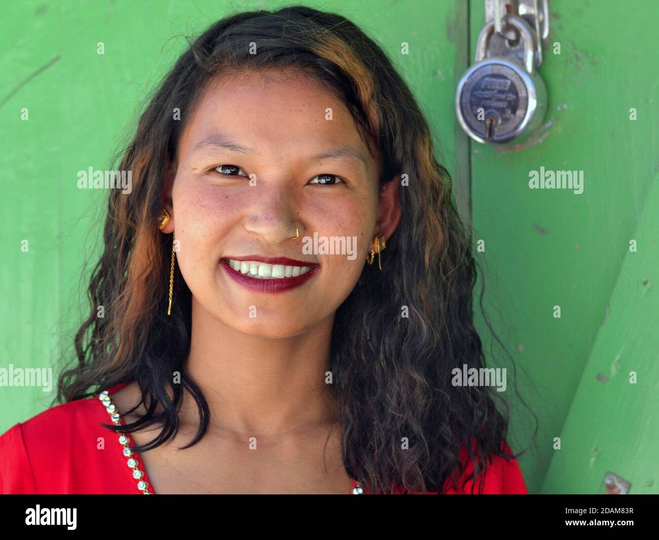 Schöne junge asiatische Frau mit rotem Lippenstift und langen Haaren Posen für die Kamera vor einer geschlossenen grünen Tür mit Vorhängeschloss. Stockfoto
