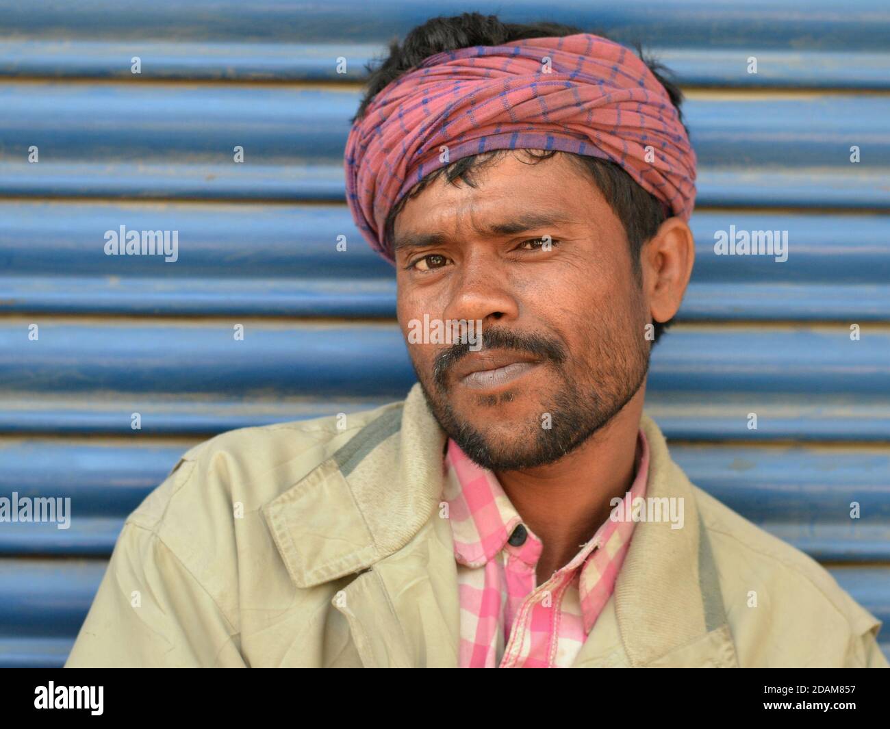 Die indische Wanderarbeiterin mittleren Alters trägt einen pinkkarierten Bandana-ähnlichen Kopfumhang und posiert für die Kamera. Stockfoto
