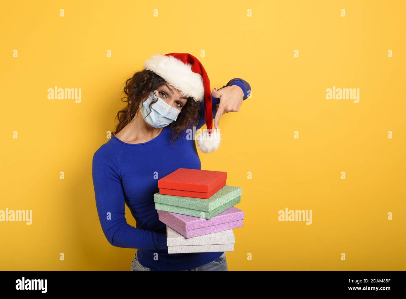 Glückliches Mädchen mit Gesichtsmaske erhält Weihnachtsgeschenke. Gelber Hintergrund Stockfoto