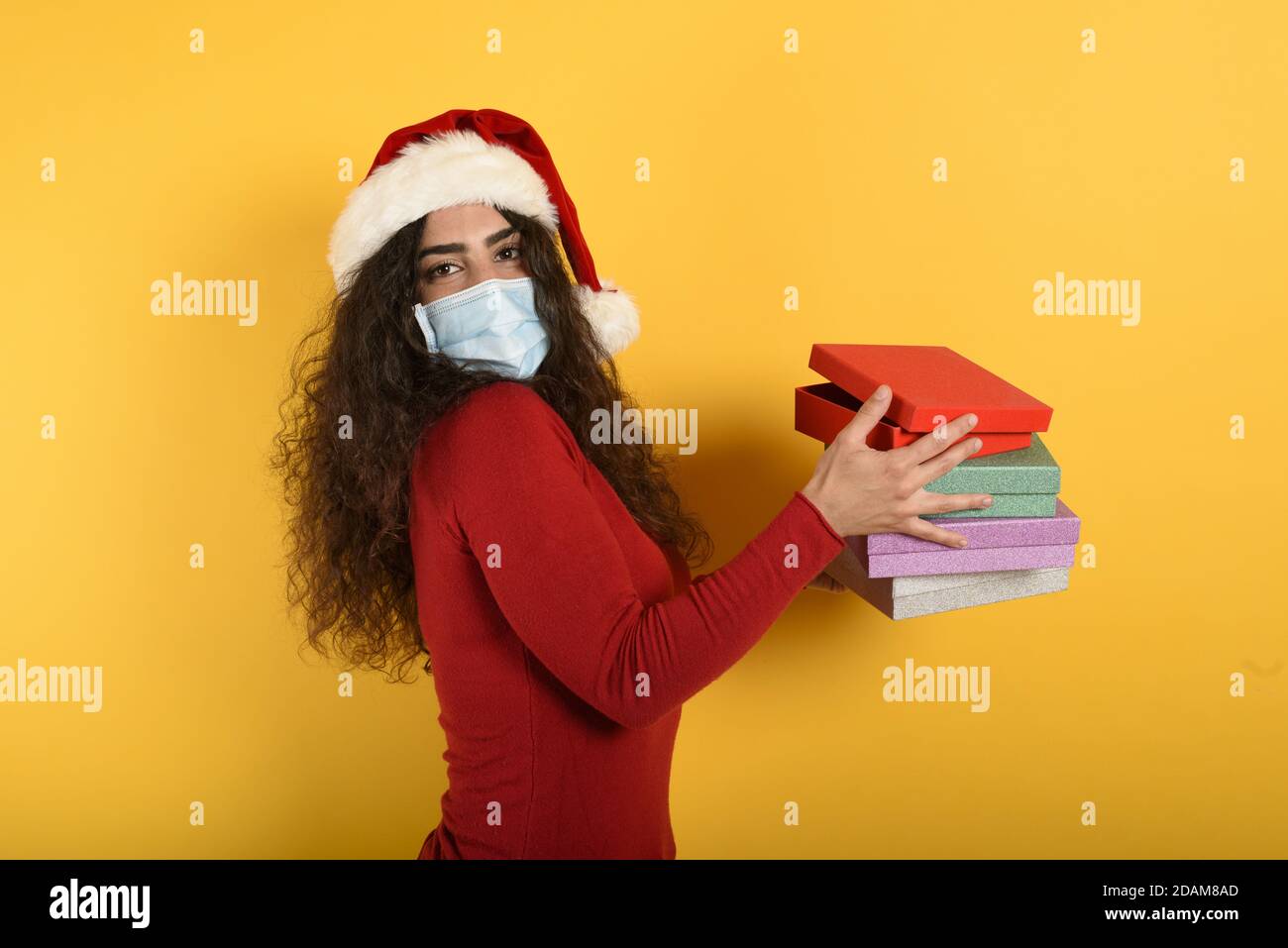 Glückliches Mädchen mit Gesichtsmaske erhält Weihnachtsgeschenke. Gelber Hintergrund Stockfoto