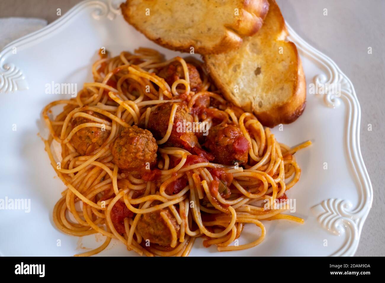 Gekochte Spaghetti und Fleischbällchen auf einem weißen Teller mit geröstetem Knoblauchbrot. Nahaufnahme. Stockfoto