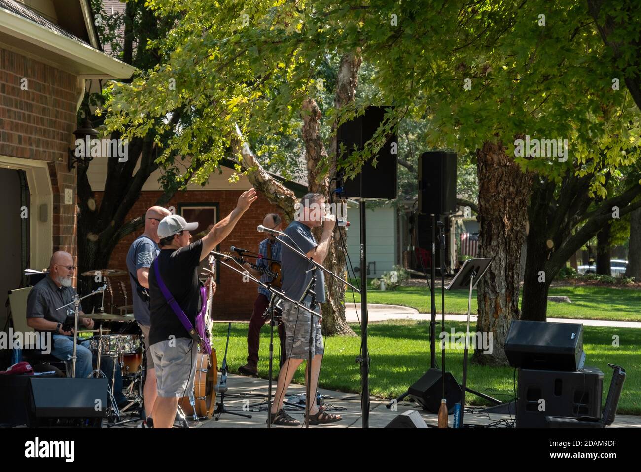 Erwachsene Männer spielen in einer Garagenband und üben für einen Gig auf einer Auffahrt vor einer Garage im Sommer. Stockfoto