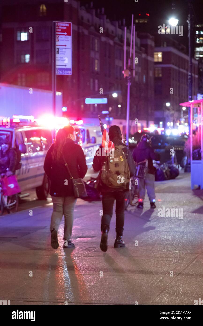 Fußgänger, die mit der amerikanischen Flagge gegen NYPD Van und Polizei Lichter bei Nacht, Greenwich Village, New York City, New York, USA Stockfoto
