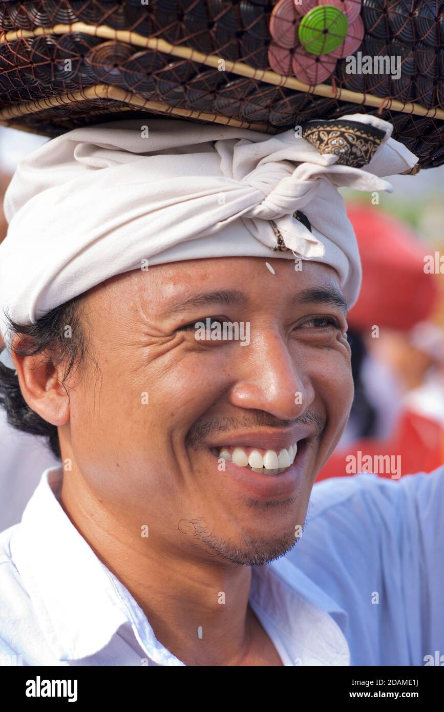 Porträt eines balinesischen Gläubigen in einem Hindu-Tempel, nahe Bali, Indonesien. Gekleidet in traditionelle weiße Kleidung mit Kopftuch und mit einem Tempelopfer Stockfoto