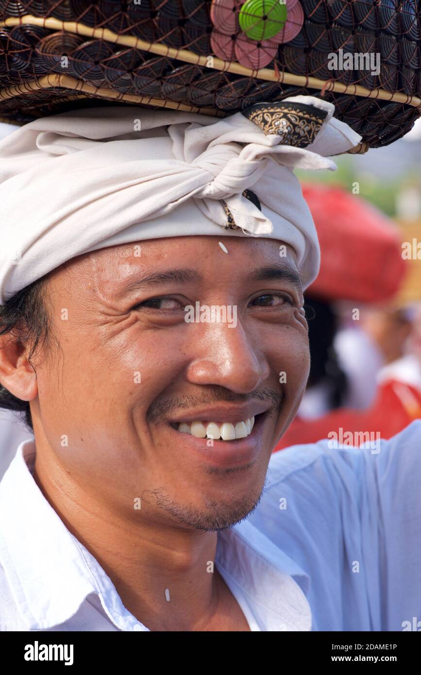 Porträt eines balinesischen Gläubigen in einem Hindu-Tempel, nahe Bali, Indonesien. Gekleidet in traditionelle weiße Kleidung mit Kopftuch und mit einem Tempelopfer Stockfoto