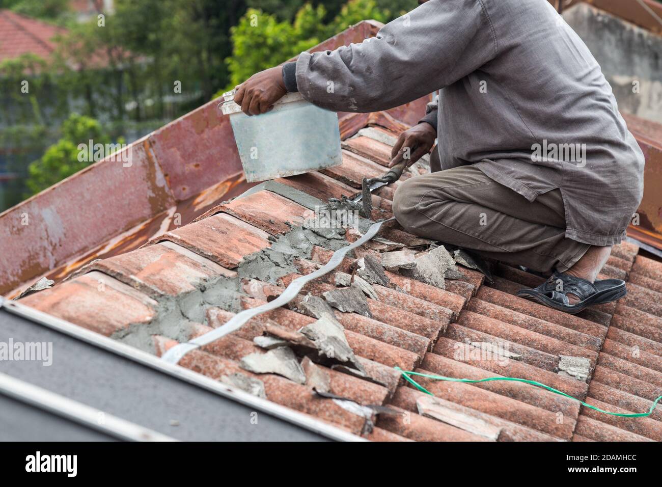 Asiatische Arbeiter sichern Dachziegel mit Zement auf dem alten Gebäude Stockfoto