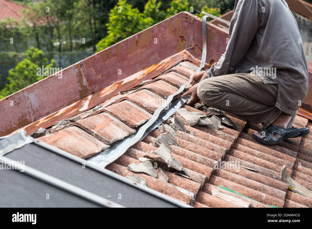 Asiatischer Arbeiter ersetzt Dachziegel des alten Wohngebäudes Stockfoto