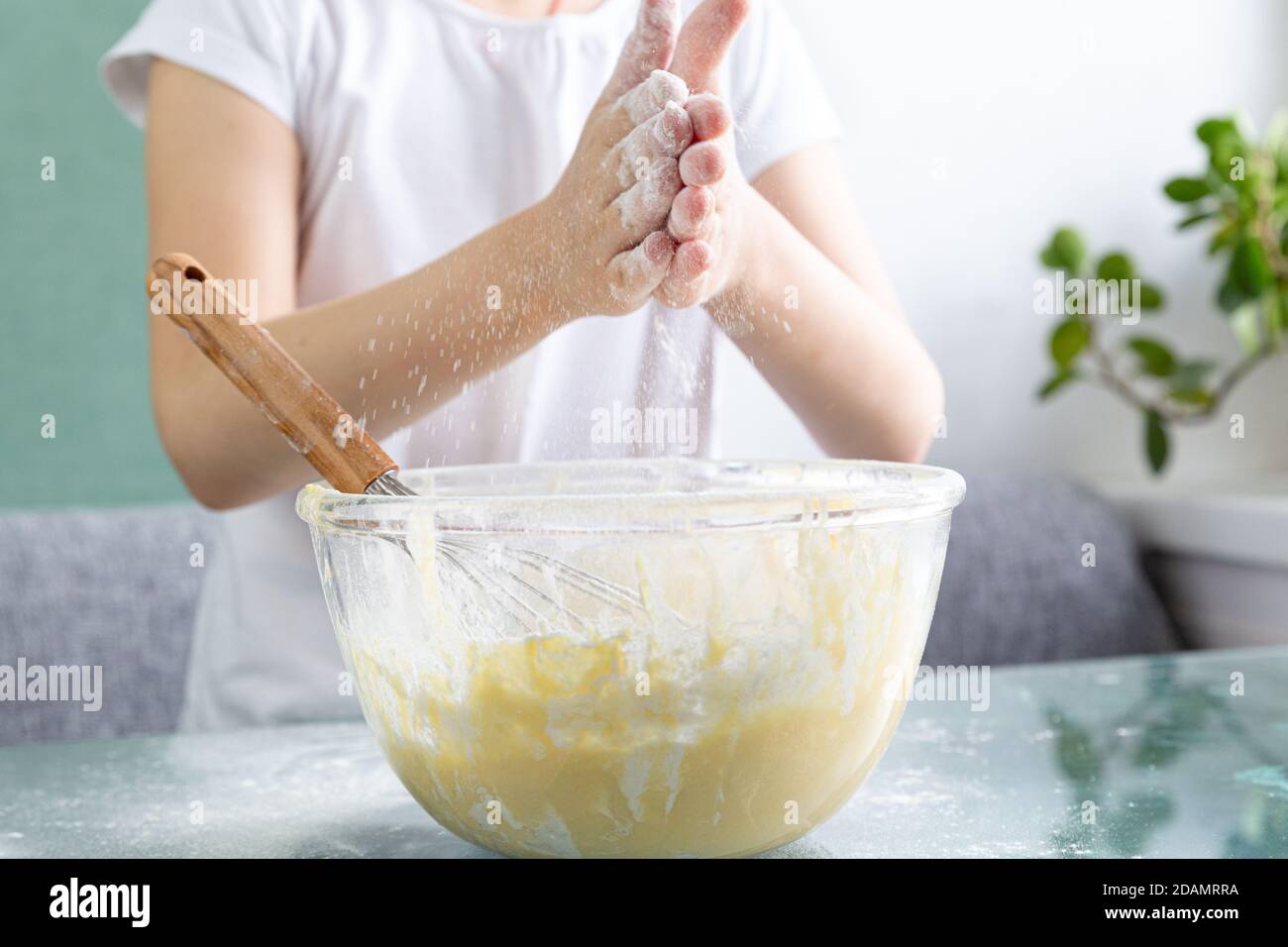 Eine Nahaufnahme des Oberkörpers eines Kindes klatscht mit den Händen über eine Schüssel Waffelteig, Mehlbrösel fliegen. Teig mit Mehl, Eiern, Milch und Zucker. Stockfoto