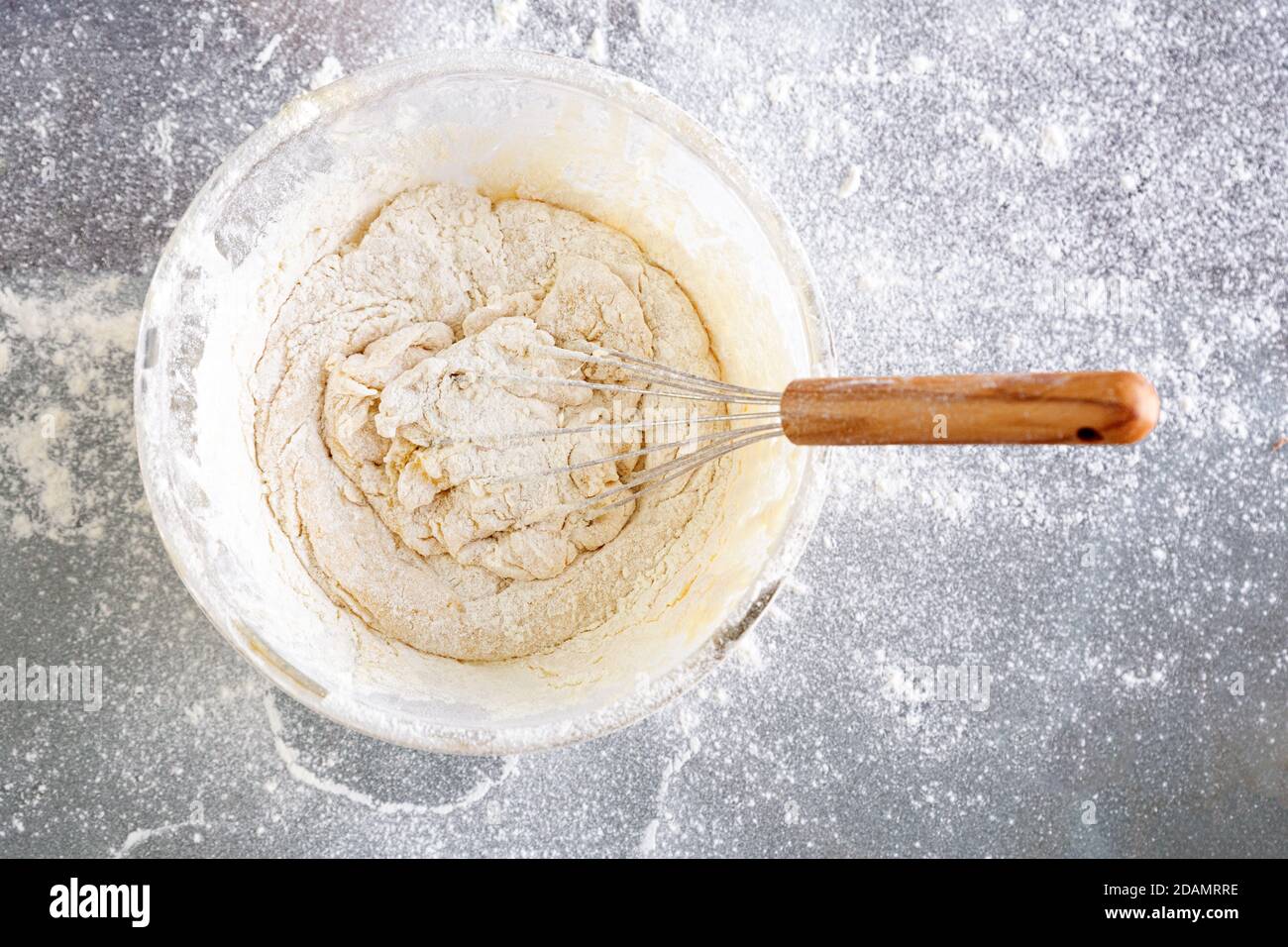 Nahaufnahme Glasschüssel mit Teig. Einen leckeren Teig mit Mehl, Eiern, Milch und Zucker schlagen. Der Teig ist fertig zum Kochen. Glastisch. Mit Mehl bestreuen. Stockfoto